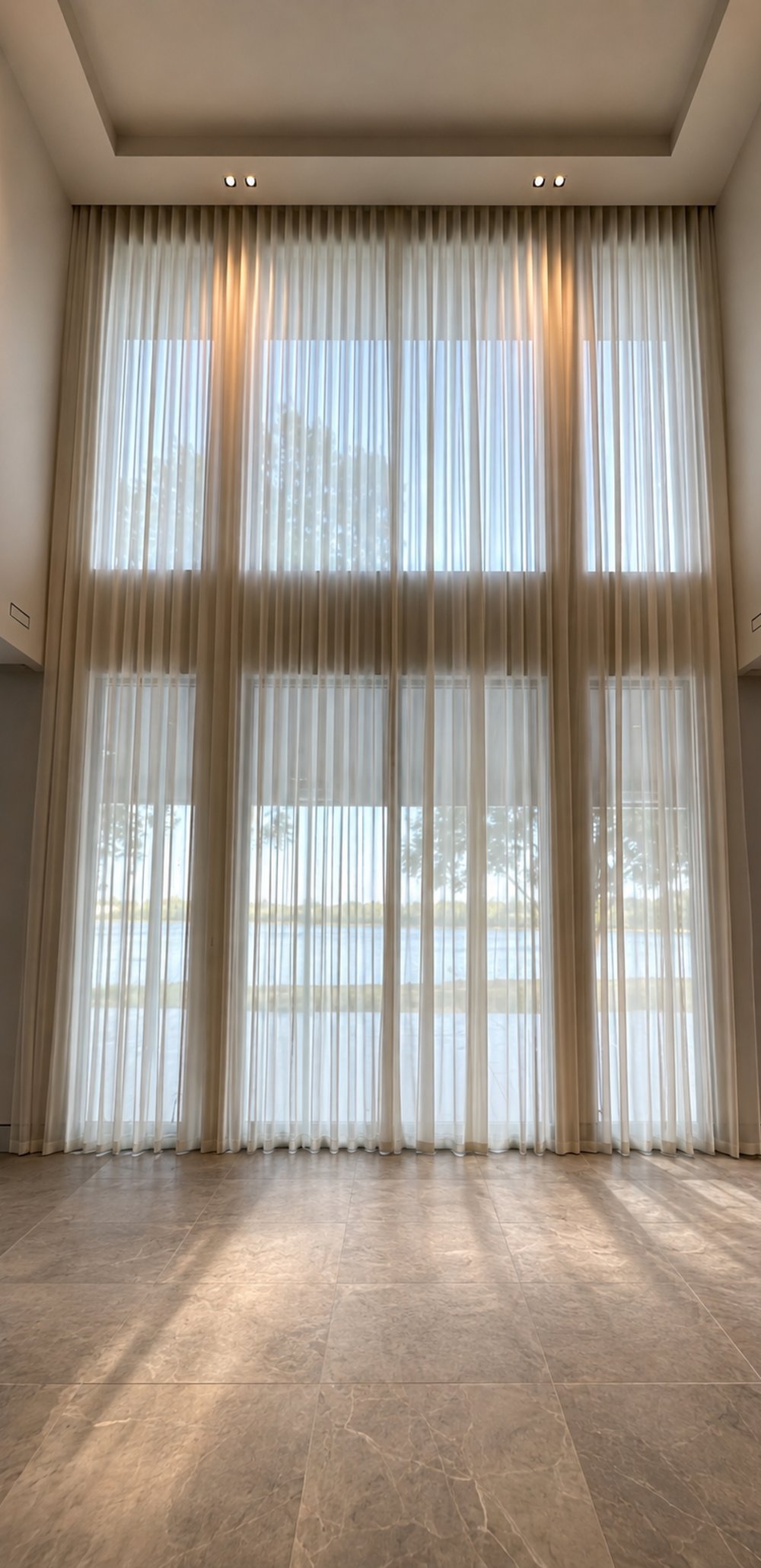 Double-height sheer wave curtains over a lake view